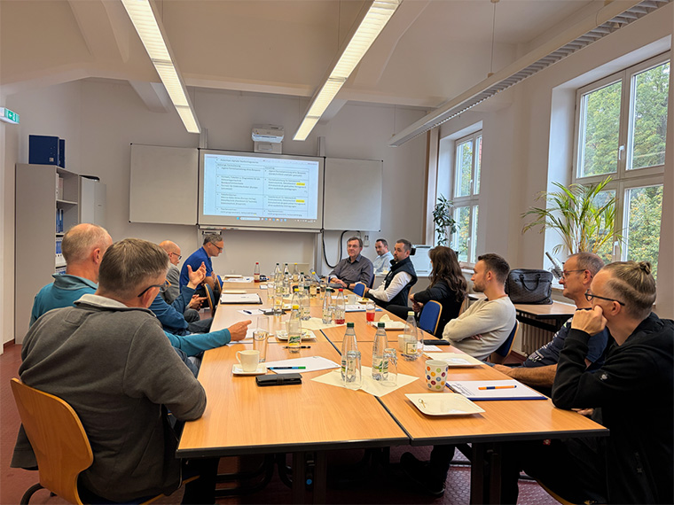 Foto: Lehrer am Tisch neben Leinwand